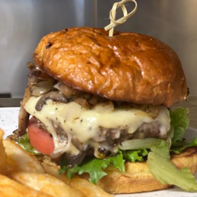 A burger with melted cheese, lettuce, tomato, and mushrooms, on a toasted bun.