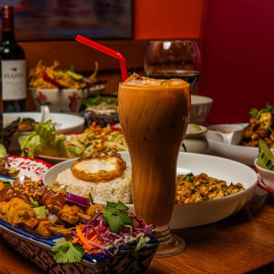Glass of Thai Iced Tea served on the table alongside various dishes.