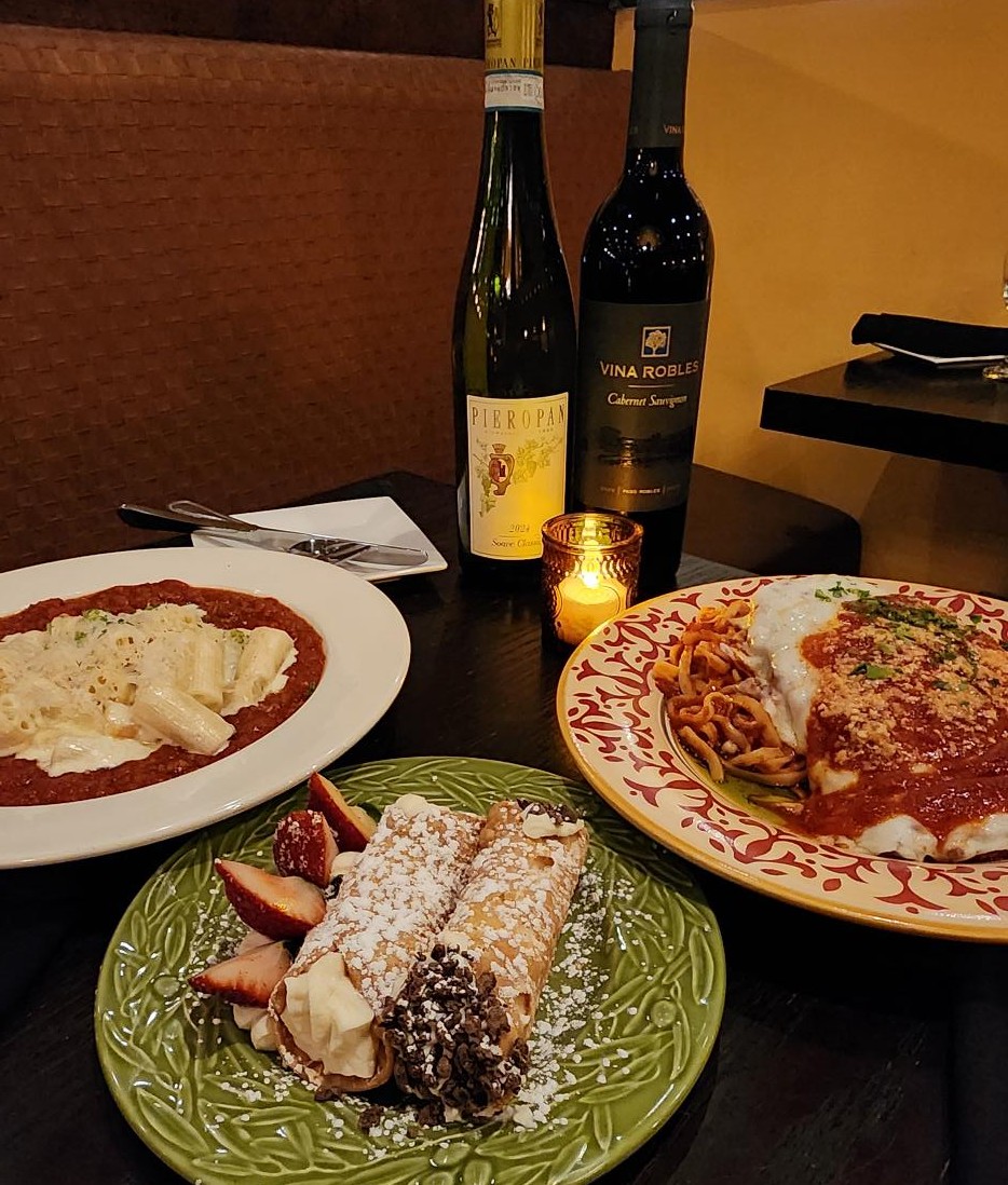A picture of two entrees, a dessert and a two bottles of wine.