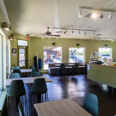Interior with sage green walls, light wood-topped tables and dark green chairs.