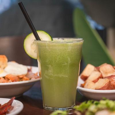 Fresh-squeezed juice garnished with a cucumber slice, surrounded by breakfast dishes.