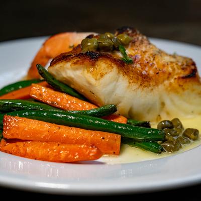 Chilean Seabass filet served with green beans and carrots, garnished with capers.