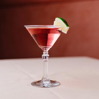 Glass of Cosmo on a white table with red background.