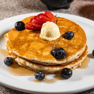 Pancakes is topped with fresh strawberries, blueberries, and a scoop of butter.