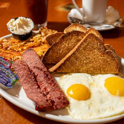 Breakfast plate featuring fried eggs, sausages, toasted wheat bread, and hash browns.