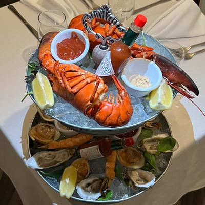 A seafood iced tower featuring a whole lobster, shrimp, oysters, and lemon wedges.
