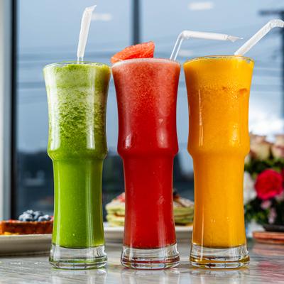 Three different colored fresh juices served in tall glasses with straws.