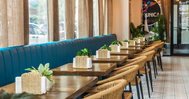 Interior - a blue cushioned bench, wooden tables, baskets with plants on each table; beige curtains