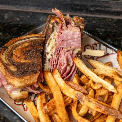 Reuben sandwich with sauerkraut on marble white bread, accompanied by crispy fries.