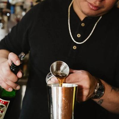 A bartender pouring liquor from a jigger into a shaker.