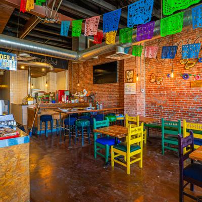 Dining area with tables, colorful chairs, brick wallsy, hanging baners and a counter.