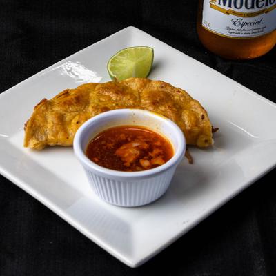 Quesabirria taco with dipping broth and lemon wedge.