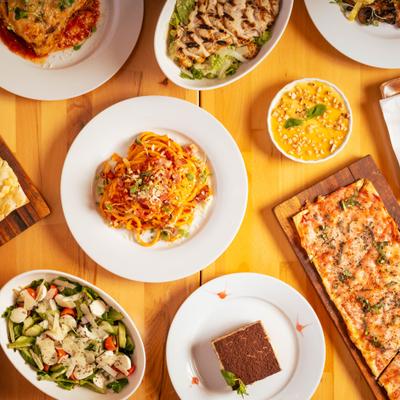 Assorted dishes on table including pasta, salads, tiramisu, and pizza.