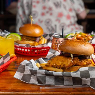 Two fried chicken burgers served in baskets with fries and colorful cocktails.