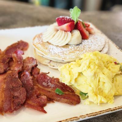 Pancakes topped with strawberries and bananas, served with bacon and scrambled eggs.