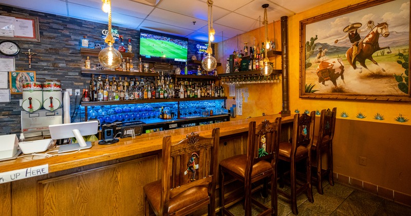 Counter, chairs, bottles on shelves, paintings, LED screen, lights