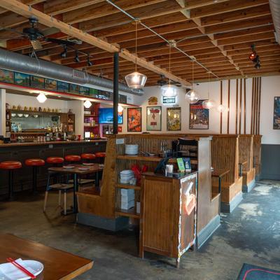 Restaurant interior with wooden booths, bar seating, and pendant lights.