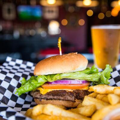 Housemade CheeseBurger with lettuce, tomato, onion garnish and french fries on the side with glass of beer in the back