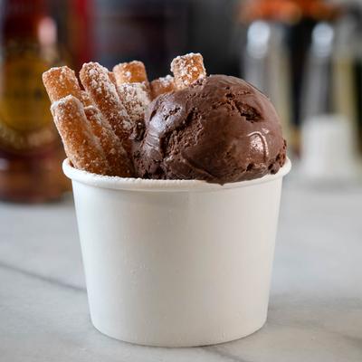Funnel cake fries served in a white cup with a scoop of chocolate ice cream.