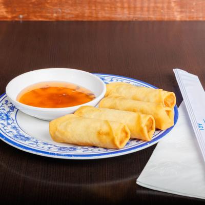 Spring rolls with dipping sauce on a blue-and-white plate beside napkins and chopsticks.