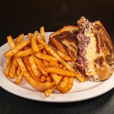 Reuben sandwich served in between rye bread with fries on the side.