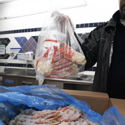 Gloved hand holding a clear bag with frozen crab legs.