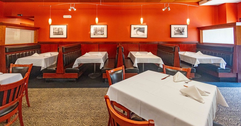 Restaurant interior with booths, white tablecloths, and framed photographs on an orange wall