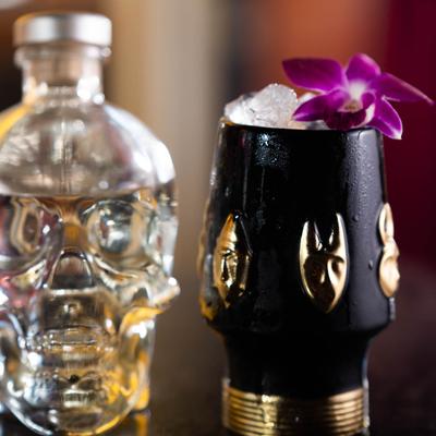 A vodka skull bottle and a black voodoo tumbler mug with a drink inside