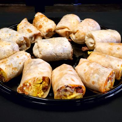 Black catering platter arranged with a variety of halved breakfast burritos.
