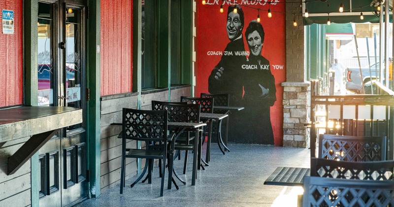 Outdoor café seating area with a mural of two figures on a red wall