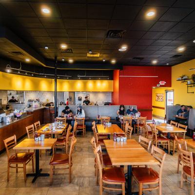 Bright restaurant interior with wooden tables, booth seating, and open kitchen area.