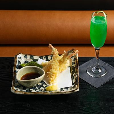 Shrimp tempura with a dipping sauce and a green cocktail on a table.