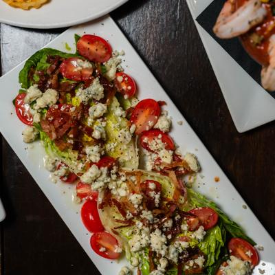 Wedge salad with baby gem lettuce, bacon, blue cheese crumbles, tomato, vinaigrette dressing.