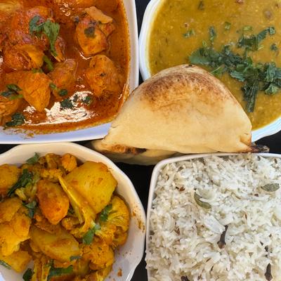 Chicken curry, aloo gobi, lentil soup, rice and naan arranged on a table.