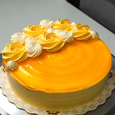 Yellow frosted mango cake featuring a glossy orange glaze and piped cream rosettes.