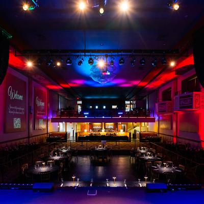 Interior, view of seating area from a stage, with red and blue lights on the walls.