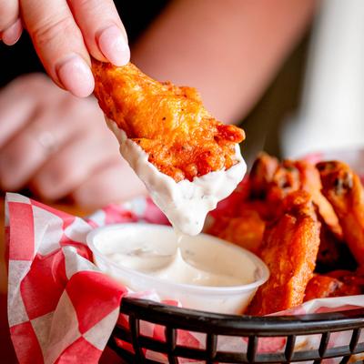 Chicken wing dipped into a cup of ranch dressing.
