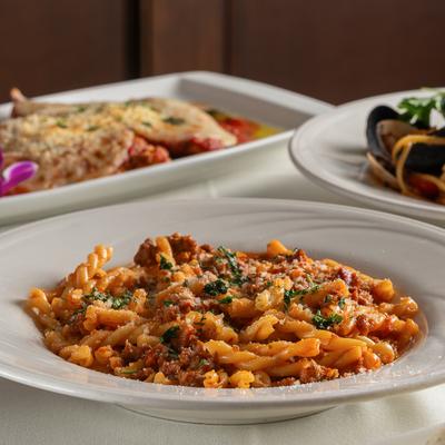 Strozzapretti pasta with meat sauce, served alongside other dishes in the background.