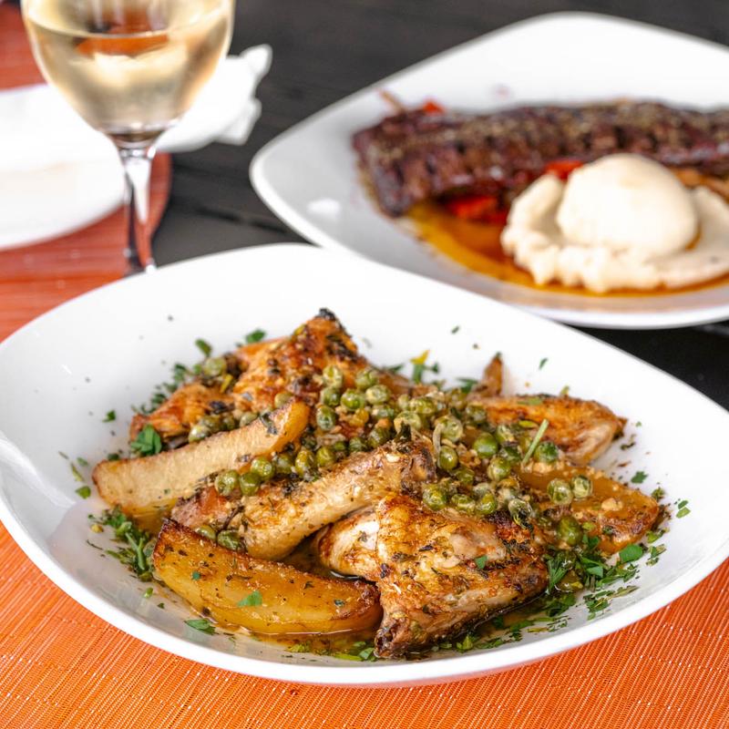 Chicken Vesuvio dish served on a white plate. accompanied with white wine