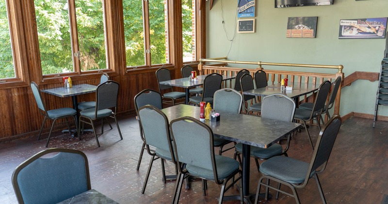 Dining area with tables, chairs, large windows, and signage on the wall