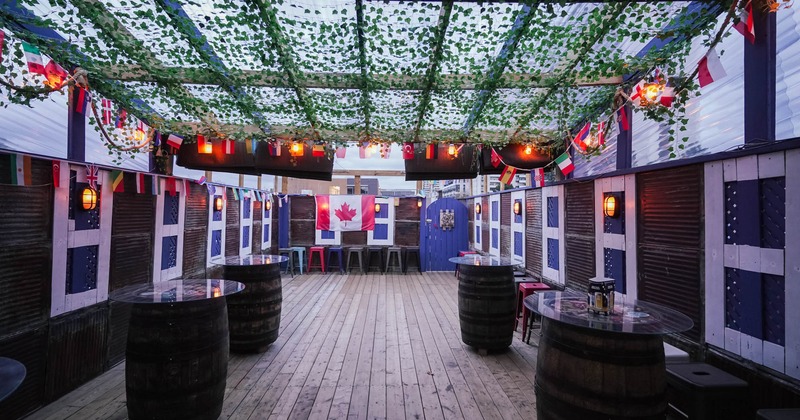 Outdoors, patio space with covered roof, barrel tables and bar chairs