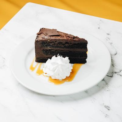A slice of chocolate cake, served with whipped cream and  caramel drizzle.