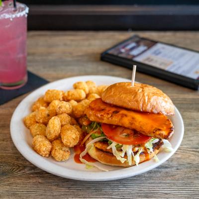 Acadian Chicken Sandwich served with tater tots and a cocktail.