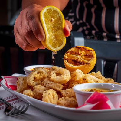 A hand squeezes lemon juice over Calamari plate with two sauces.