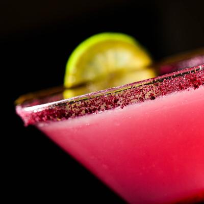 Extreme close up shot of a pink cocktail served in a martini glass with lime garnish.