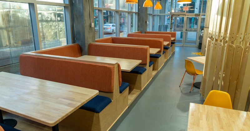 Modern dining area with wooden booths, orange and blue seating, orange pendant lights, yellow chairs