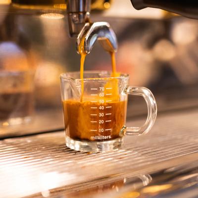 Machine pouring espresso into a measuring cup.