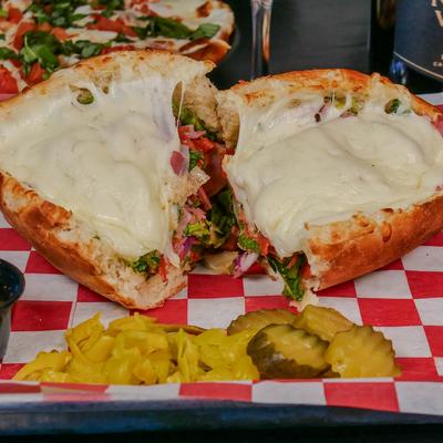 Italian submarine sandwich covered in melted cheese served with pickles.