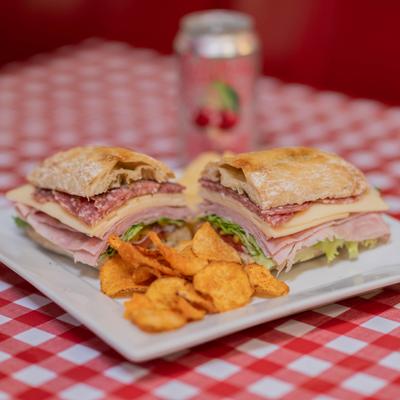 Antipasto Supreme sandwich served with potato chips and a canned drink.