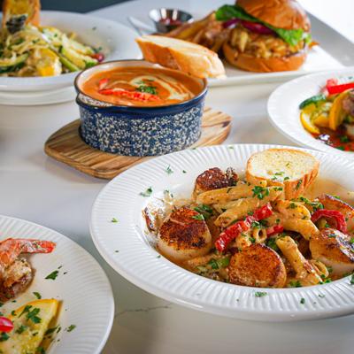 Seafood pasta with scallops, lobster bisque soup, and burger with fries on a table.